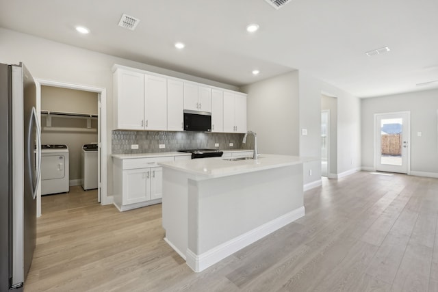 kitchen featuring washing machine and clothes dryer, appliances with stainless steel finishes, tasteful backsplash, a sink, and light wood-type flooring