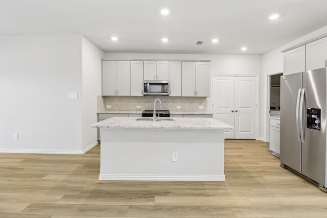 607 Willet Dr, Mckinney, TX 75069 - kitchen with appliances with stainless steel finishes, decorative backsplash, a center island with sink, and light wood-type flooring