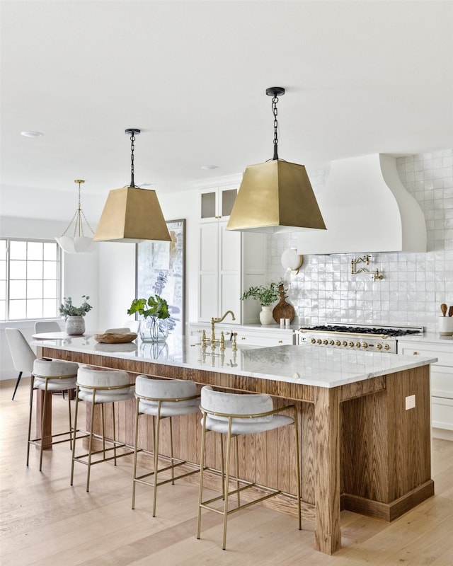 kitchen featuring decorative backsplash, custom exhaust hood, stove, light stone counters, and light wood-style flooring