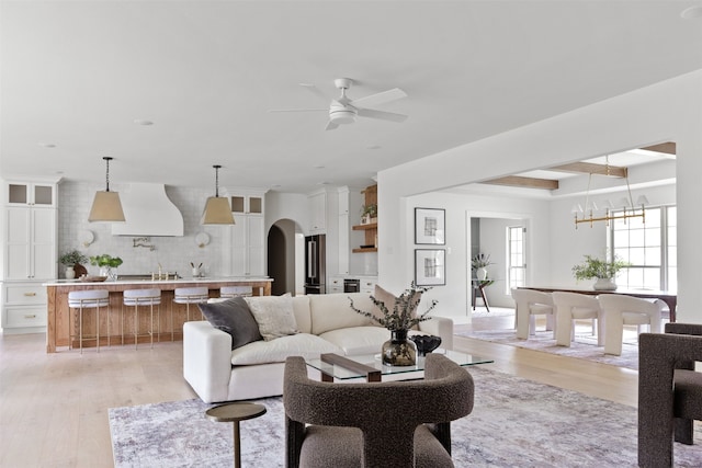 living area with arched walkways, light wood-style flooring, and ceiling fan with notable chandelier
