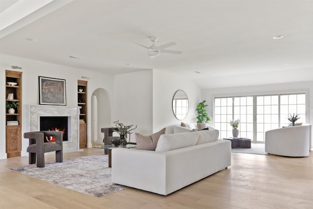 living room featuring light wood-type flooring, arched walkways, a ceiling fan, and a fireplace