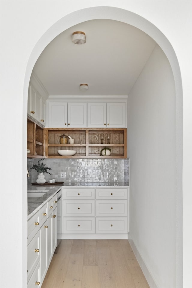 bar featuring a sink, dishwasher, arched walkways, light wood-style flooring, and backsplash