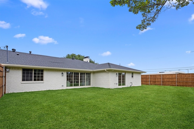 rear view of house featuring brick siding, a chimney, a yard, and fence private yard