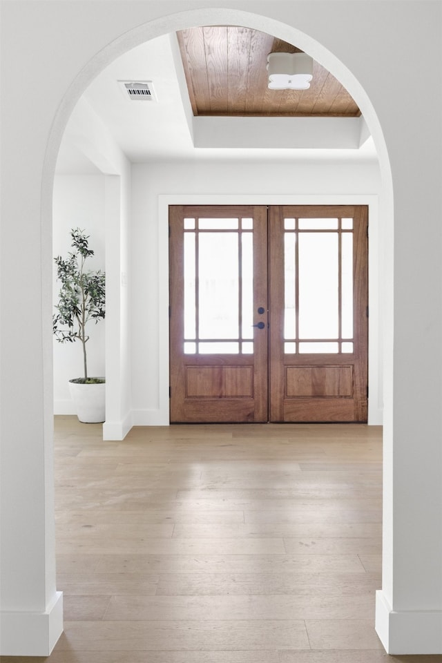 entrance foyer featuring french doors, visible vents, baseboards, a tray ceiling, and hardwood / wood-style floors