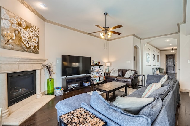 living area with a premium fireplace, arched walkways, a ceiling fan, wood finished floors, and ornamental molding