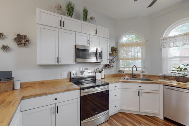 kitchen with ceiling fan, white cabinetry, a sink, stainless steel appliances, and butcher block countertops
