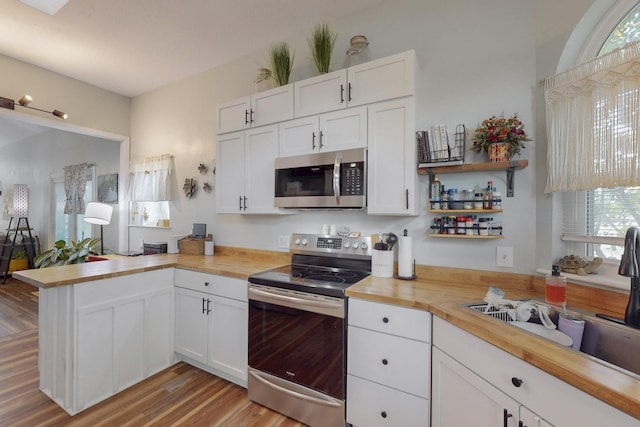 kitchen with stainless steel appliances, wood counters, white cabinetry, and a peninsula