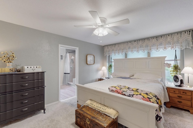 bedroom featuring baseboards, ensuite bathroom, light carpet, and ceiling fan