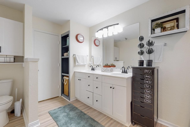 bathroom featuring double vanity, toilet, a sink, and wood finished floors