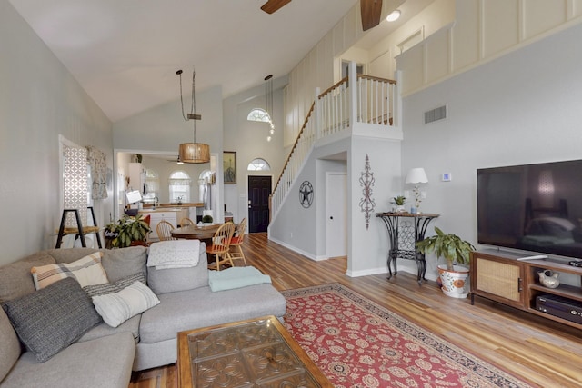 living area featuring high vaulted ceiling, stairs, a ceiling fan, wood finished floors, and visible vents