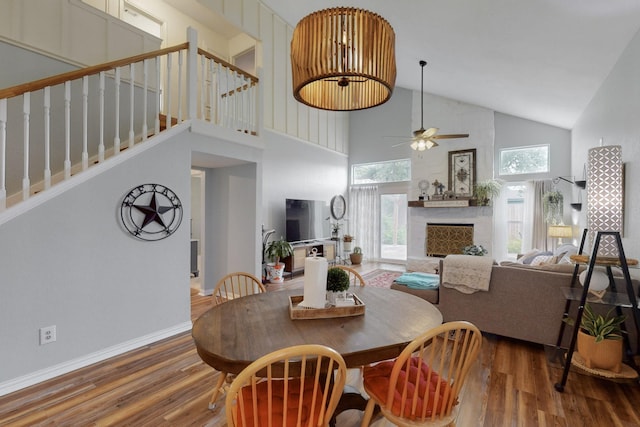 dining area featuring a fireplace, high vaulted ceiling, a ceiling fan, wood finished floors, and stairway