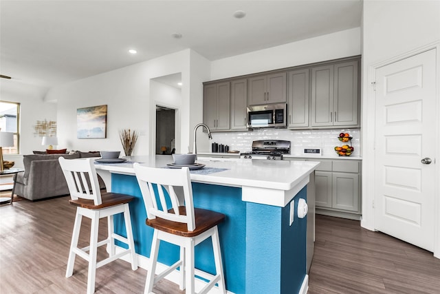 kitchen with gray cabinets, stainless steel microwave, open floor plan, gas range, and backsplash