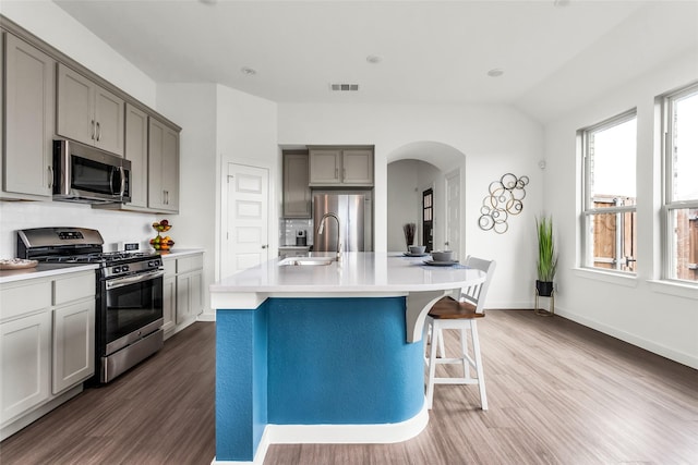 kitchen featuring dark wood-style flooring, arched walkways, gray cabinetry, light countertops, and stainless steel appliances