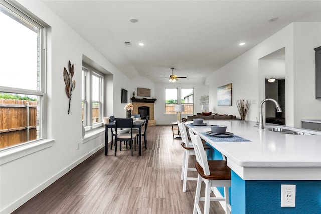 kitchen featuring wood finished floors, a fireplace, ceiling fan, light countertops, and a sink
