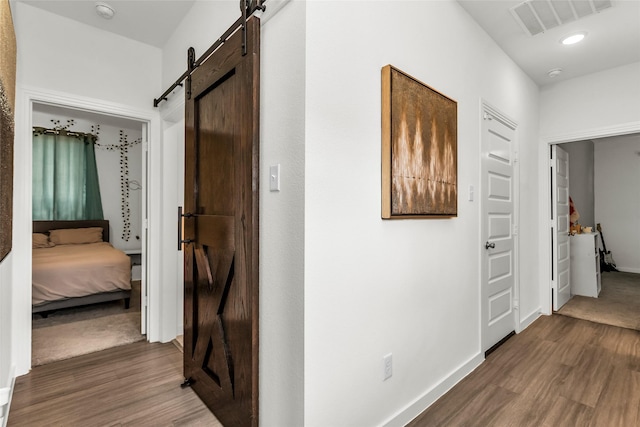 hall featuring baseboards, dark wood-style floors, a barn door, and visible vents