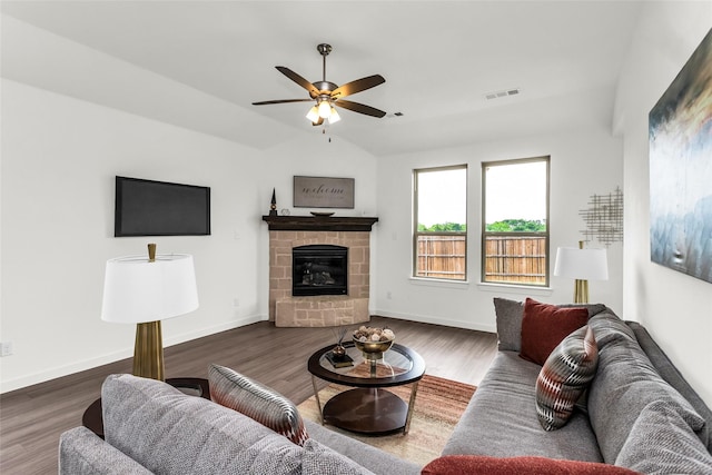 living area featuring visible vents, wood finished floors, a stone fireplace, a ceiling fan, and vaulted ceiling
