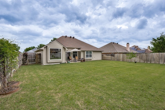 rear view of property with a fenced backyard, a shingled roof, a yard, and a patio area