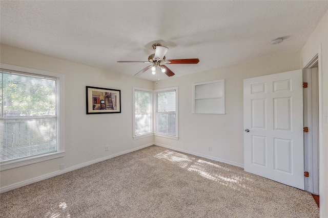 carpeted spare room with a healthy amount of sunlight, baseboards, and ceiling fan
