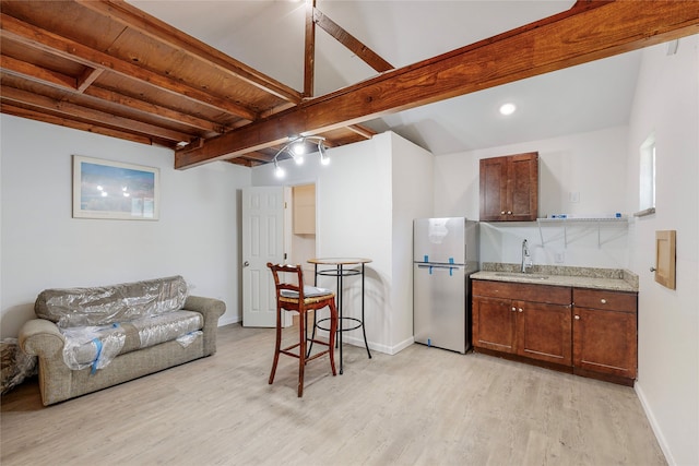 kitchen with freestanding refrigerator, beam ceiling, baseboards, a sink, and light wood finished floors