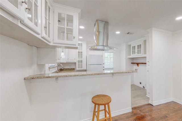 kitchen featuring visible vents, freestanding refrigerator, a peninsula, wood finished floors, and island exhaust hood