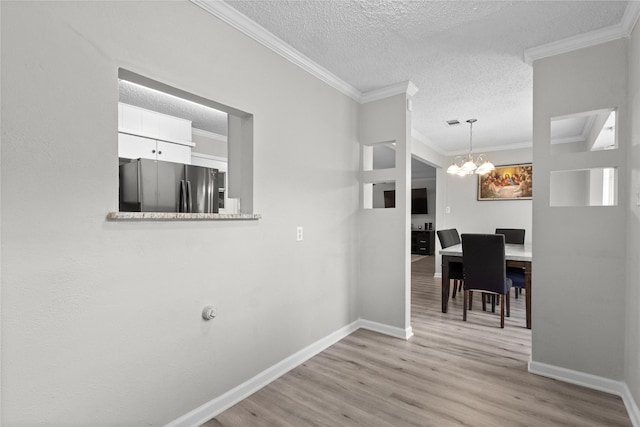 unfurnished dining area with a textured ceiling, baseboards, a chandelier, ornamental molding, and light wood-style flooring