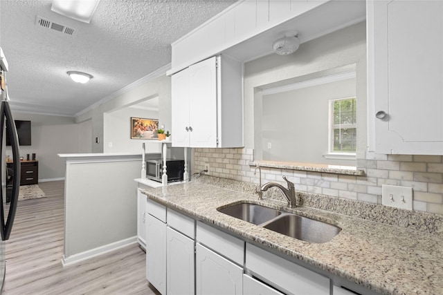 kitchen featuring a sink, light wood-style floors, white cabinetry, tasteful backsplash, and visible vents