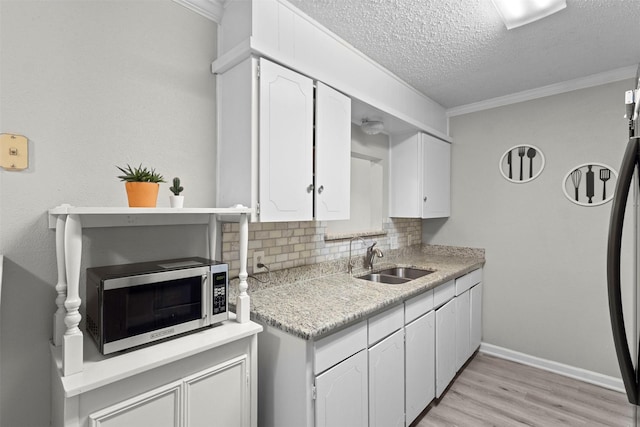 kitchen featuring white cabinets, backsplash, stainless steel microwave, and a sink