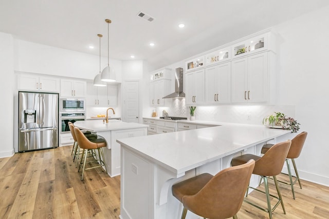 kitchen featuring wall chimney range hood, a kitchen bar, light wood-type flooring, tasteful backsplash, and appliances with stainless steel finishes