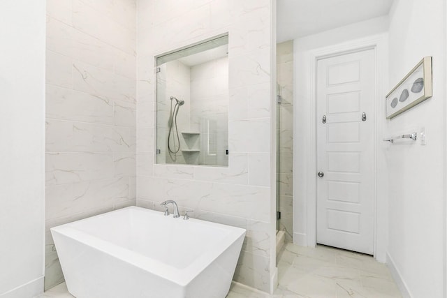 full bathroom with marble finish floor, tile walls, baseboards, a freestanding bath, and a stall shower