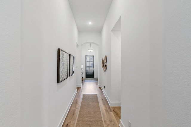 hall with light wood-style floors, arched walkways, baseboards, and recessed lighting