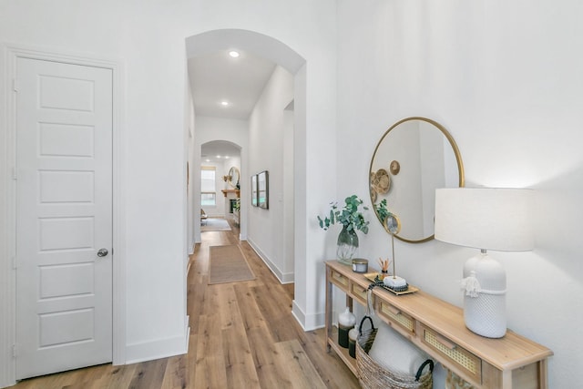 corridor with recessed lighting, arched walkways, baseboards, and light wood finished floors
