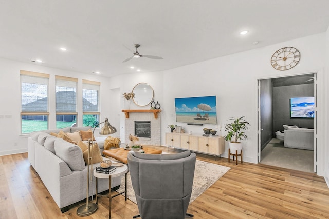 living area featuring a brick fireplace, ceiling fan, and light wood-style floors