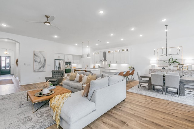 living room with baseboards, arched walkways, light wood-style flooring, and ceiling fan with notable chandelier