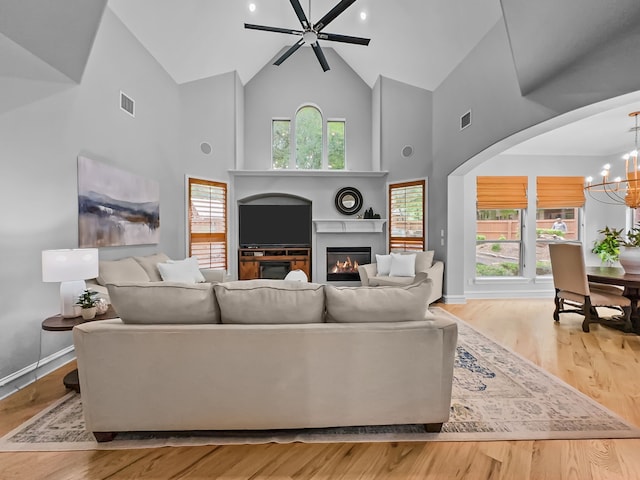 living room featuring visible vents, a glass covered fireplace, ceiling fan with notable chandelier, and high vaulted ceiling