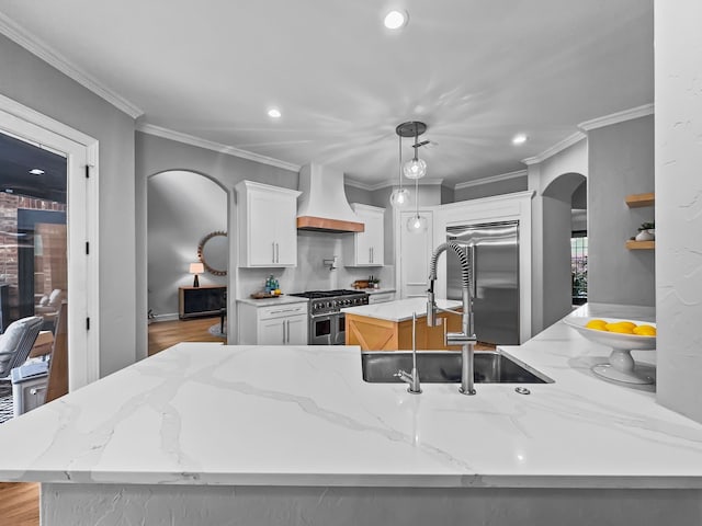 kitchen featuring a kitchen island with sink, double oven range, arched walkways, a sink, and custom range hood