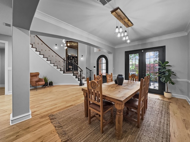 dining area featuring light wood finished floors, arched walkways, french doors, stairs, and visible vents