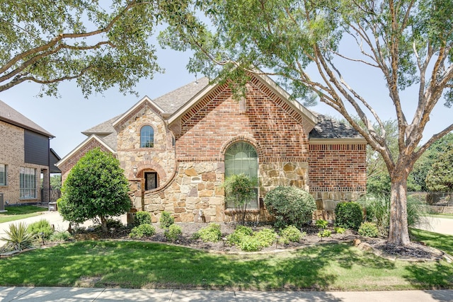 view of front of property featuring roof with shingles, brick siding, stone siding, and a front lawn