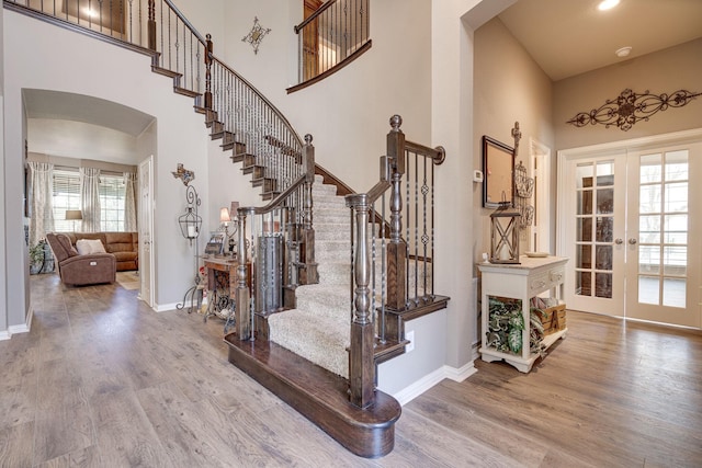 staircase featuring arched walkways, a high ceiling, french doors, and wood finished floors