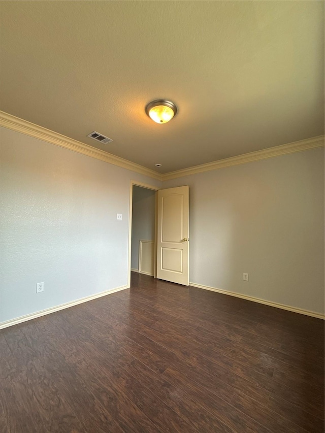 empty room with visible vents, dark wood finished floors, crown molding, and baseboards