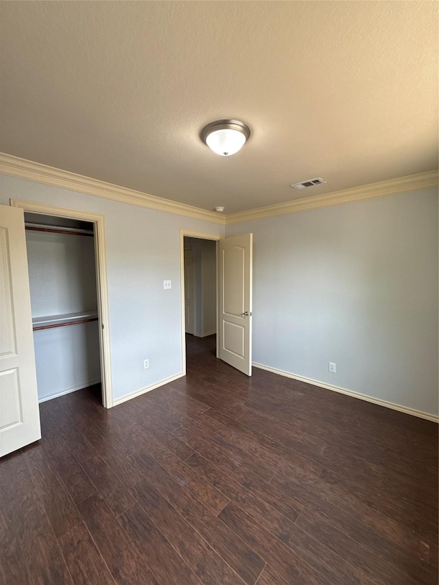 unfurnished bedroom featuring crown molding, baseboards, dark wood-type flooring, visible vents, and a closet