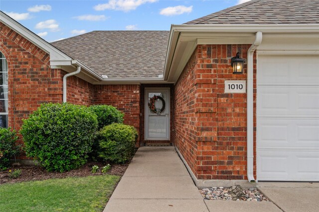 entrance to property featuring roof with shingles, brick siding, and a garage