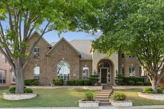 view of front of home featuring a shingled roof, a front lawn, and brick siding