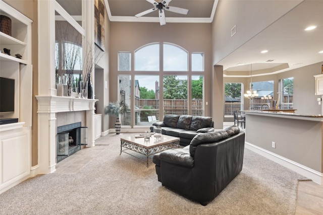 carpeted living area featuring a tiled fireplace, ceiling fan with notable chandelier, baseboards, visible vents, and ornamental molding
