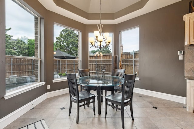 dining space featuring light tile patterned floors, a tray ceiling, an inviting chandelier, and baseboards