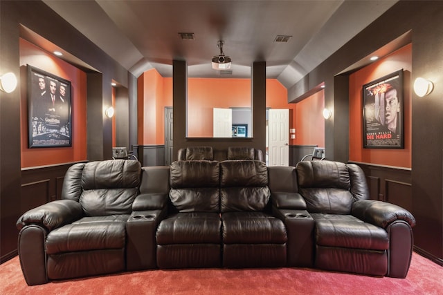 home theater room featuring visible vents, vaulted ceiling, wainscoting, a decorative wall, and carpet flooring