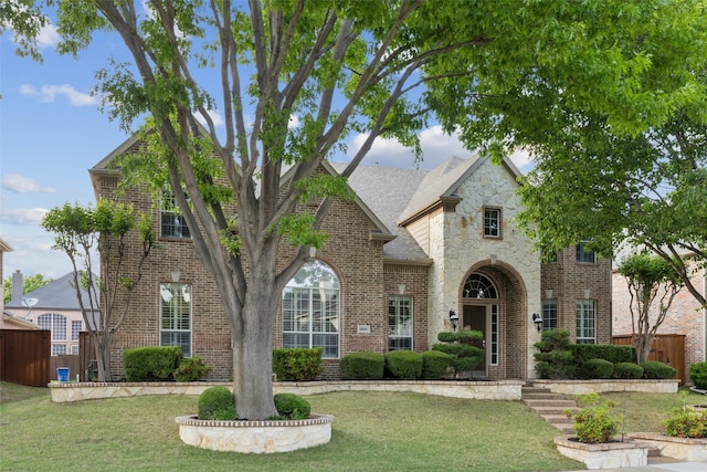 view of front of house with brick siding, a front yard, fence, and stone siding