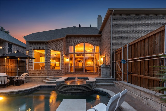 rear view of house featuring a chimney, a pool with connected hot tub, a patio area, and brick siding