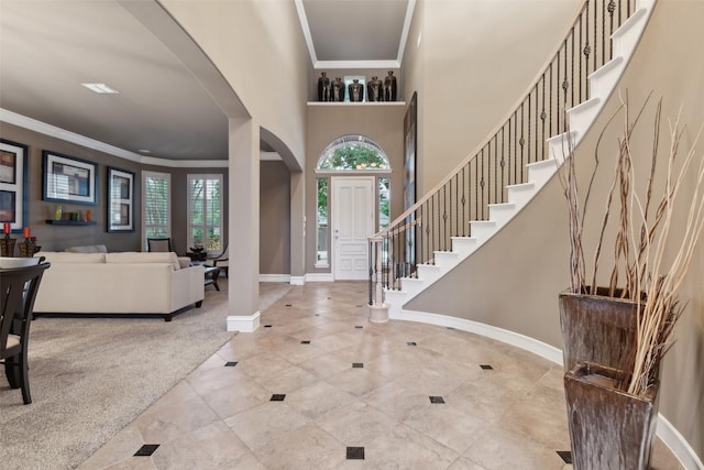 carpeted entrance foyer with crown molding, arched walkways, baseboards, and stairs