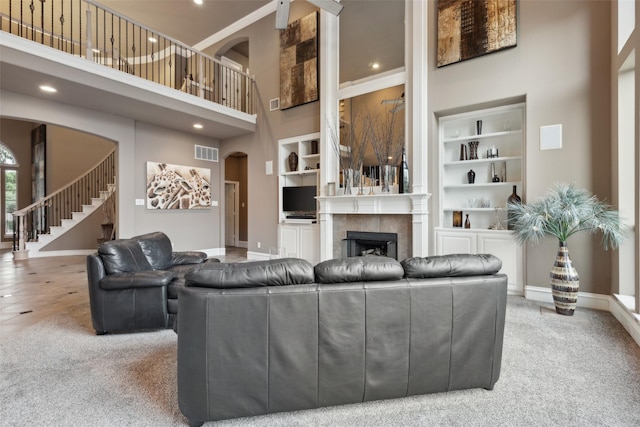 carpeted living room with visible vents, a tiled fireplace, arched walkways, built in features, and a high ceiling
