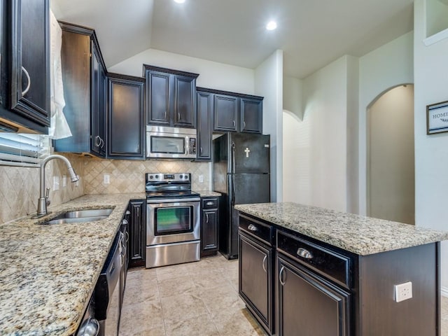 kitchen featuring appliances with stainless steel finishes, tasteful backsplash, arched walkways, a sink, and light stone counters